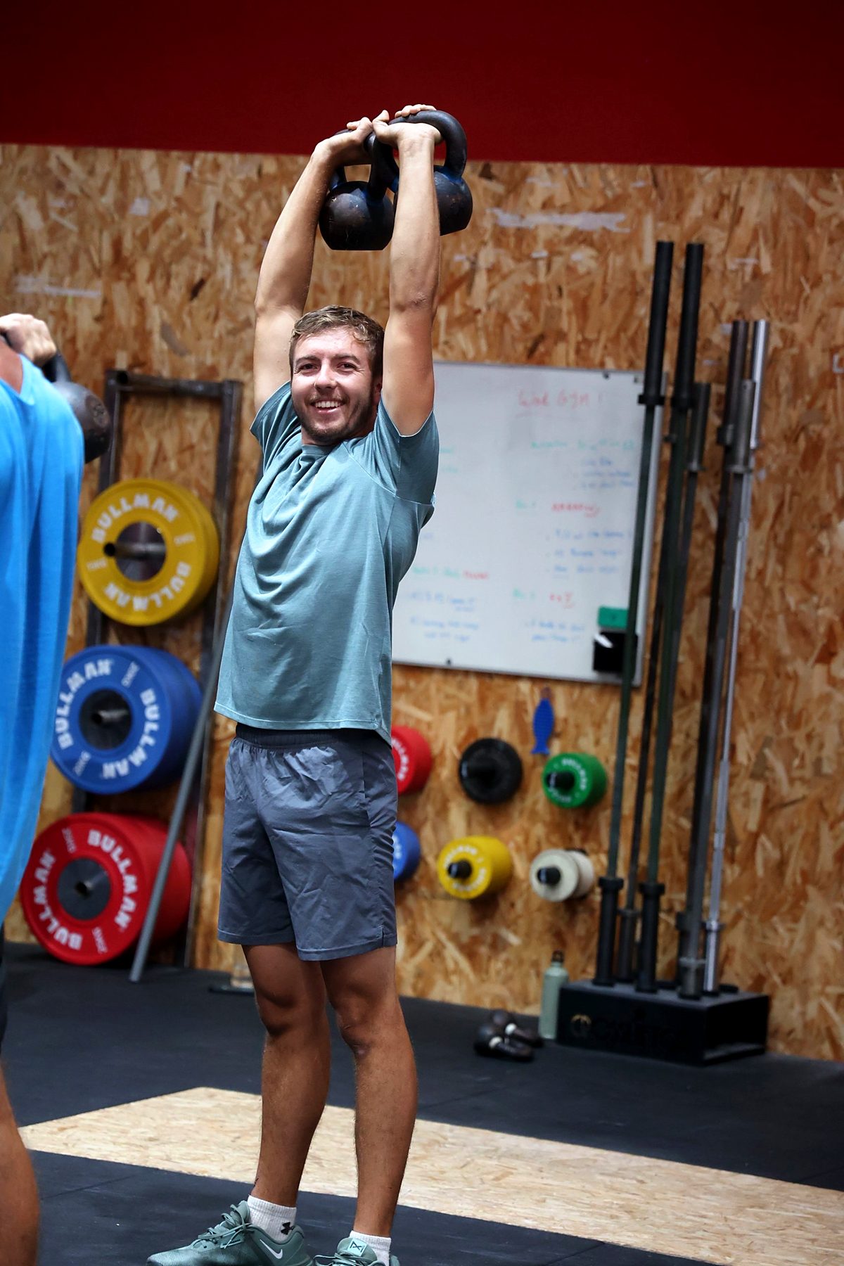 Un adhérent souriant lève deux kettlebells au-dessus de la tête